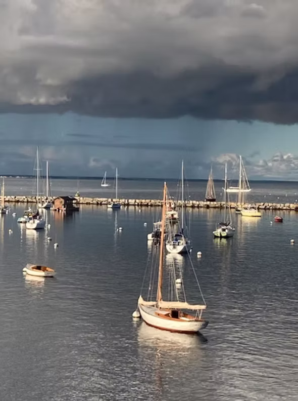Sailboats moored in the harbor under dramatic storm light